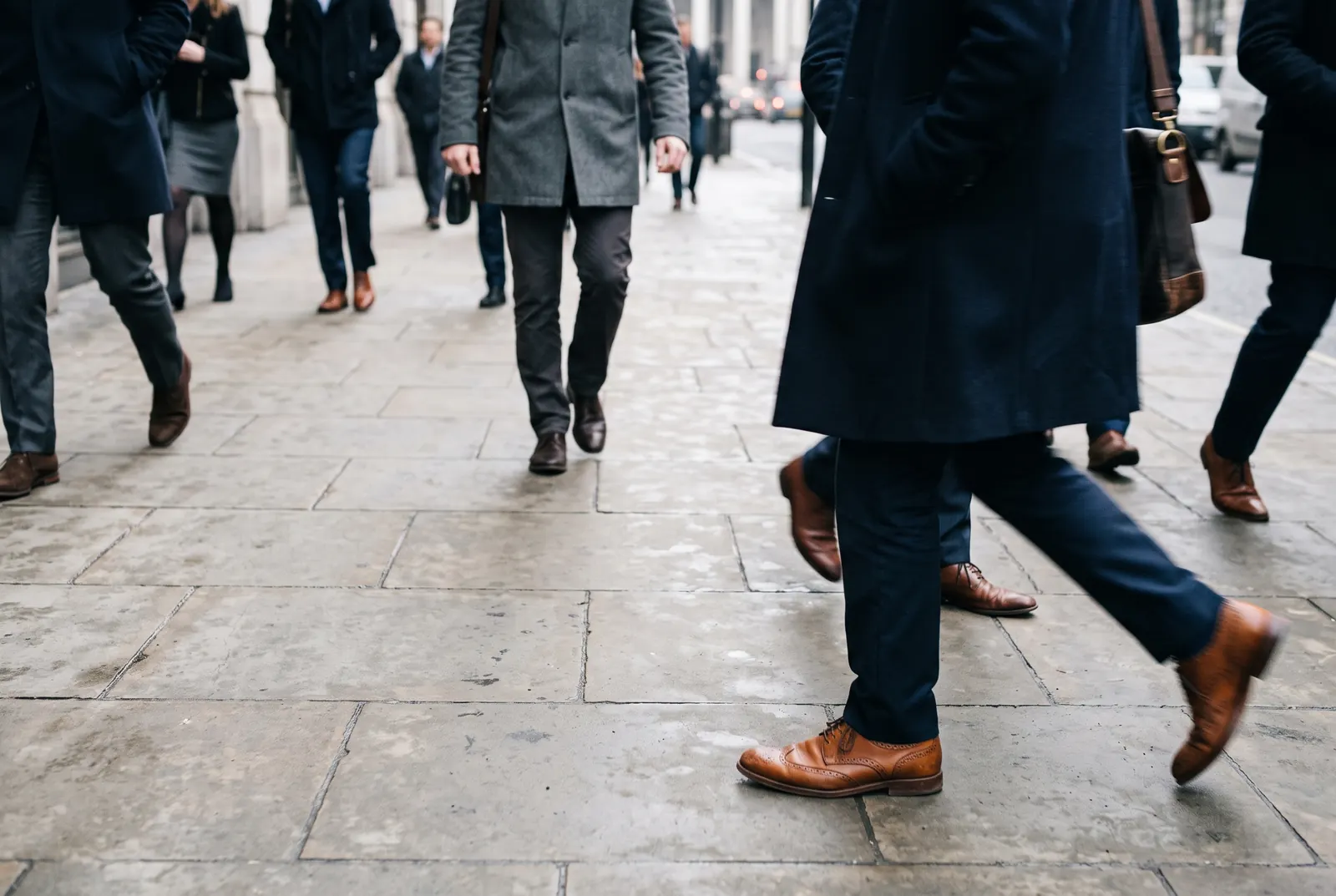 Commuters walk quickly along a city sidewalk while one person slows down